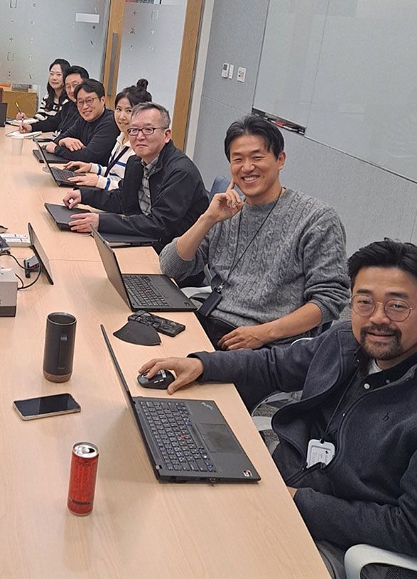 A team of people sit around a conference table with laptops, smiling and looking at the camera during a meeting.