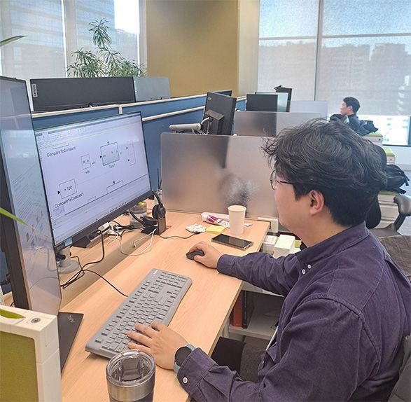 A person works at a desk with a large computer monitor displaying diagrams in a modern office environment.