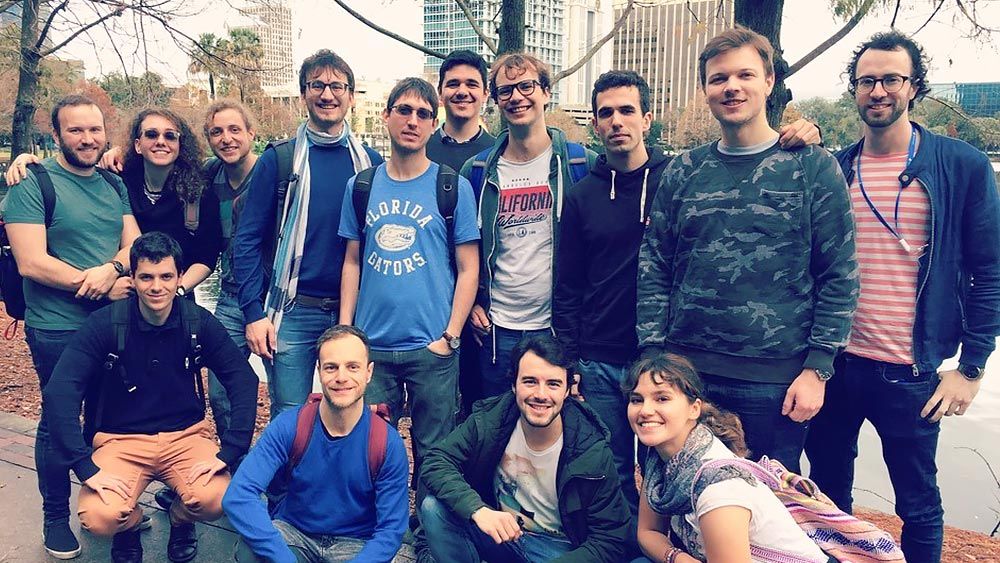 Group photo showing MathWorks staff in casual clothing with trees and buildings in the background.