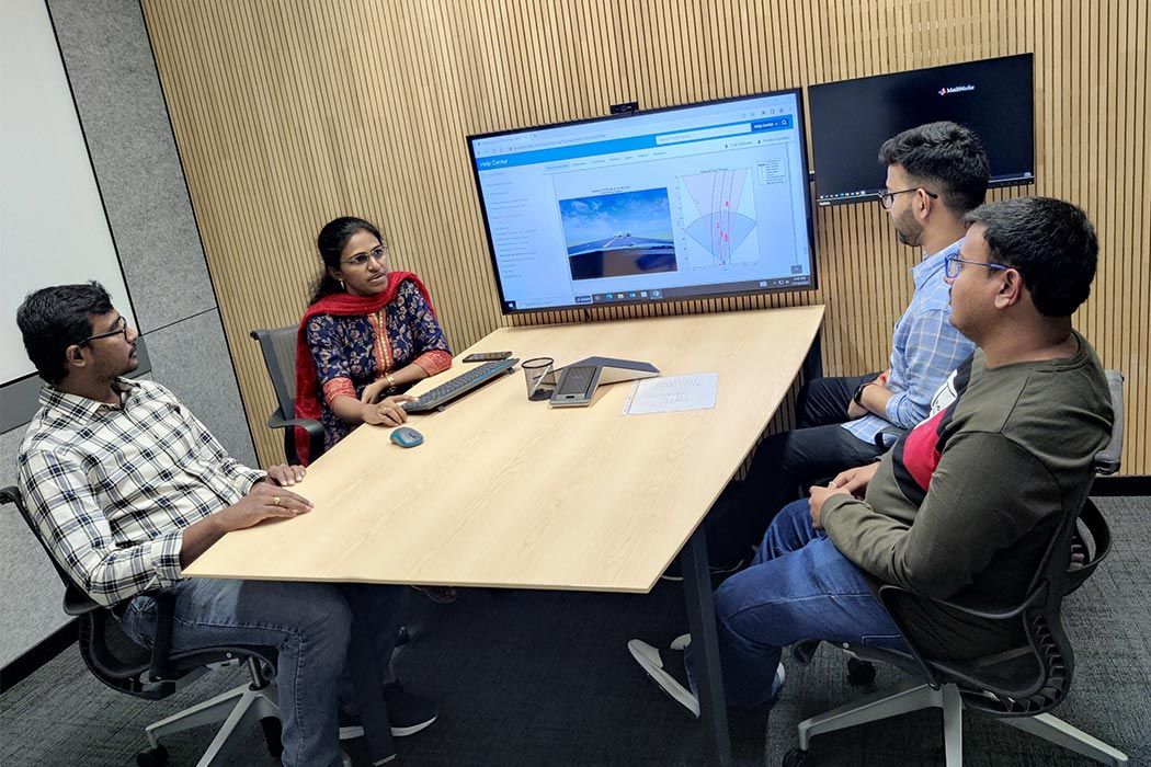 Four staff members seated in a small conference room with a large monitor displaying screenshots from RoadRunner software